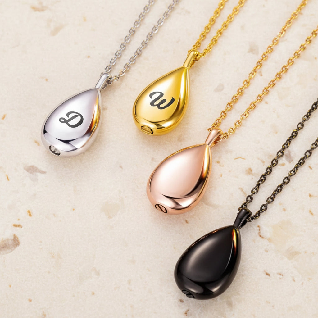 Four teardrop-shaped pendants on chains with different metallic finishes on a white background.