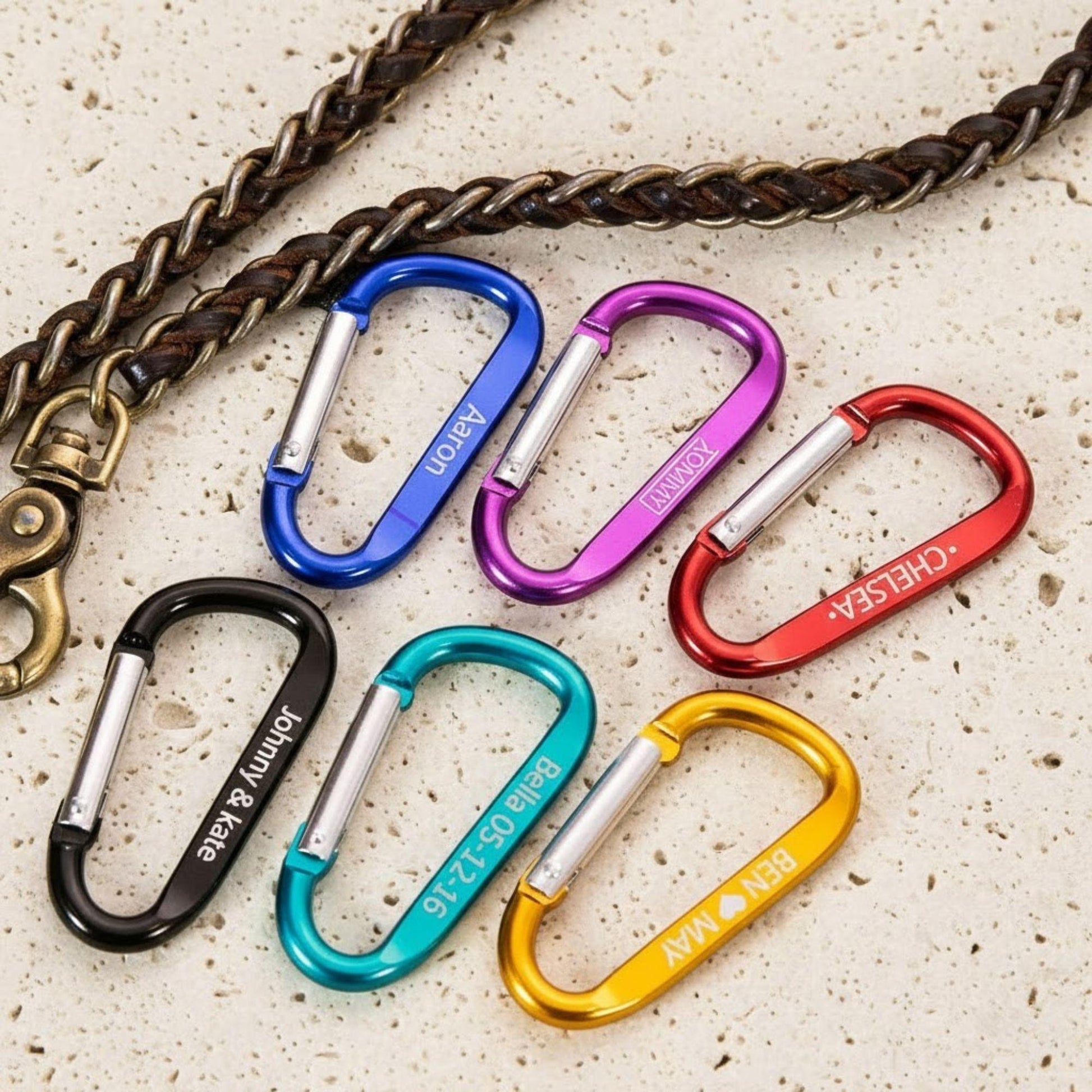 Set of colorful carabiners on a textured surface with a braided leather strap.